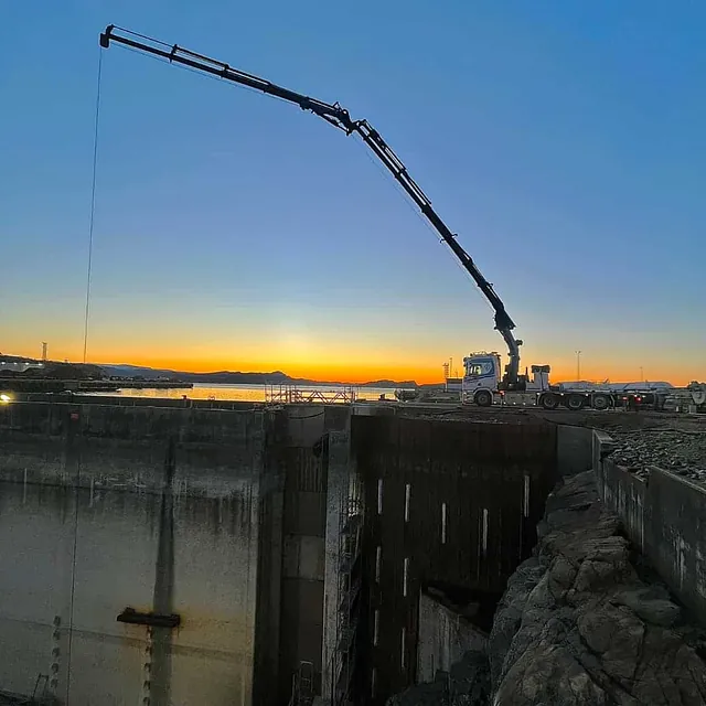 Kranbil jobber ved kai med solnedgang i bakgrunnen.