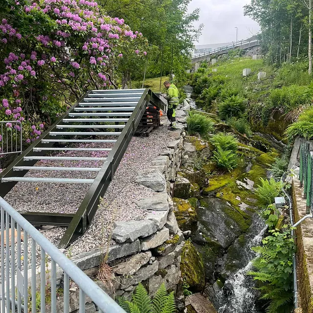 Metalltrapp monteres ved en bekk omgitt av blomster.