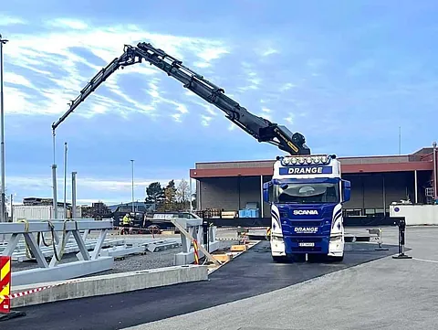Drange lastebil med utstrakt kranarm på en asfaltert plass.