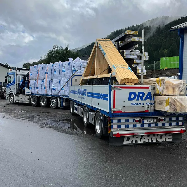 Lastebil med byggevarer parkert på våt asfalt.