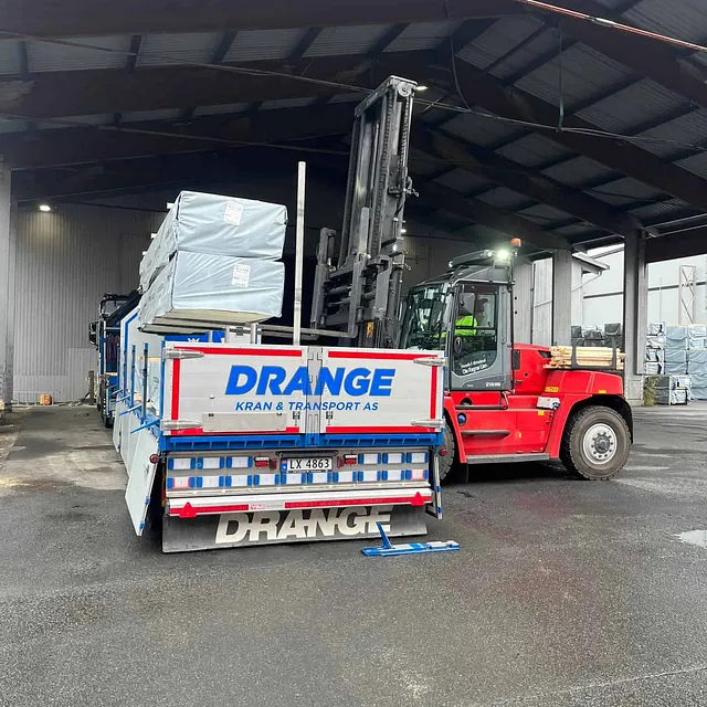 Rød gaffeltruck laster varer på en lastebil i lagerhall.