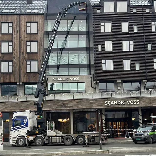 Kranbil løfter en arbeider opp til hotellfasade i Voss.